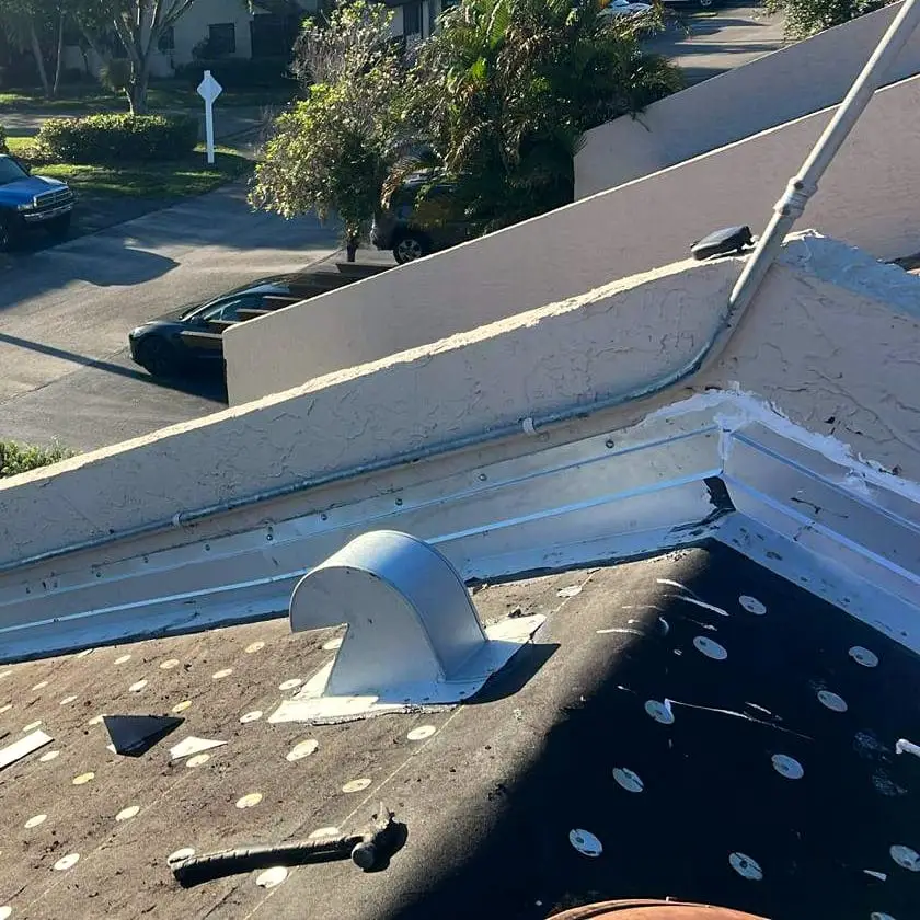 Metal flashing along a stucco parapet wall and a roof vent set into the cap-nailed underlayment