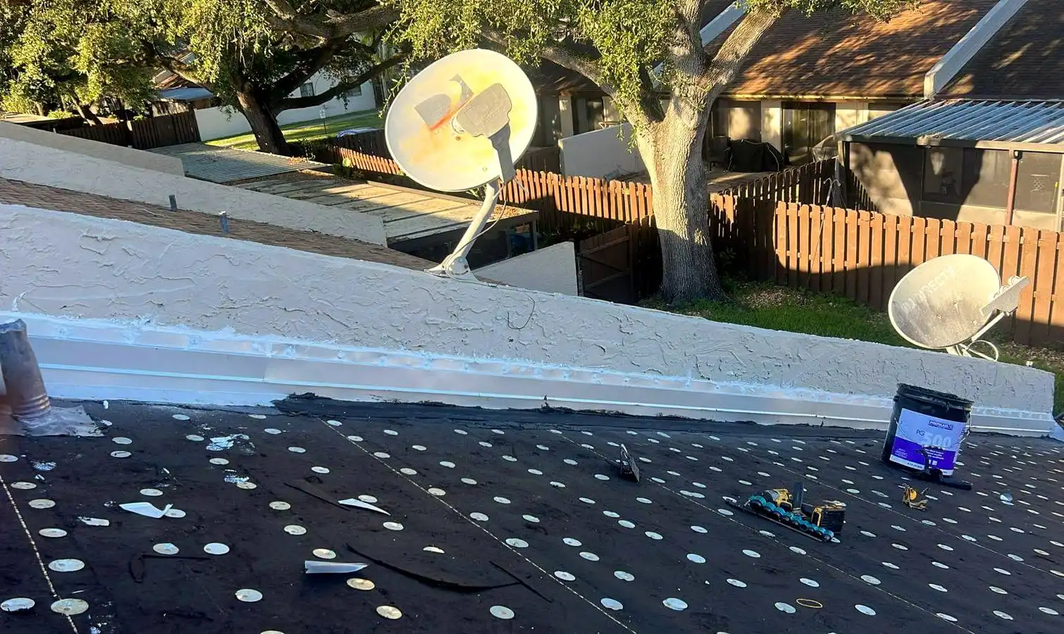Low-slope roof dried in with a base sheet fastened by rows of cap nails, beside a stucco parapet