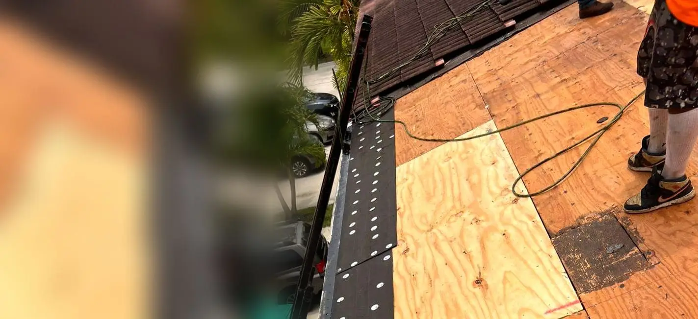 PSR crew member on a plywood roof deck, with cap-nailed underlayment along the eave and the old tile above
