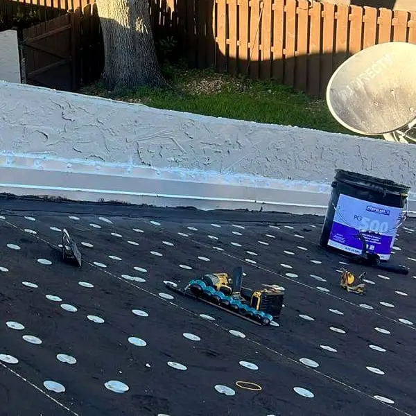 Underlayment fastened with rows of cap nails at the foot of a parapet wall, a Polyglass bucket beside it